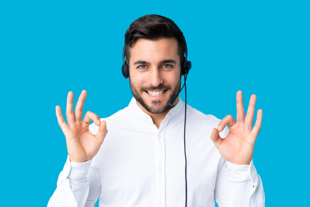 Telemarketer man working with a headset over isolated blue background showing an ok sign with fingers